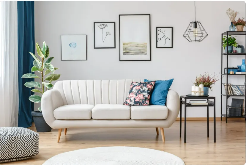 Modern living room with white sofa, floral and blue cushions, framed art, and stylish pendant lighting on accent walls.