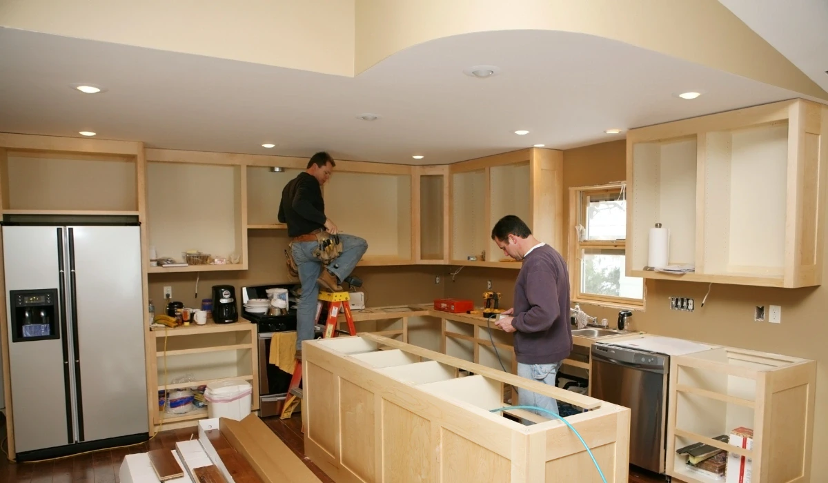 Two men installing wooden cabinets and a countertop during a modern kitchen renovation.