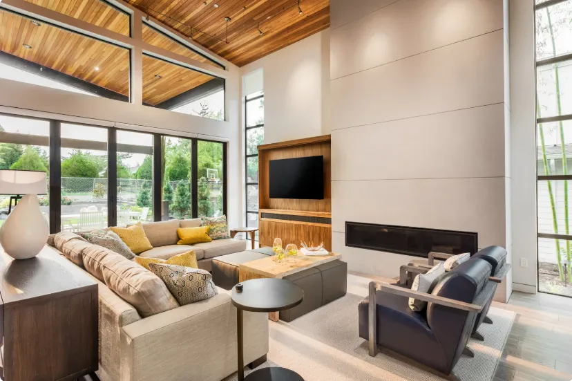 Bright modern living room with large windows, cozy seating, wooden ceiling, and sleek entertainment unit remodeling design.