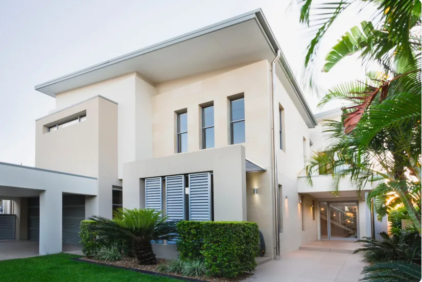 Modern two-story house with pale stone facade, large windows, and lush greenery | Home Remodeling Service