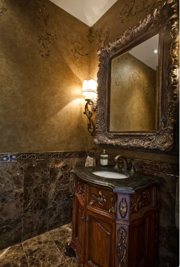 Luxurious bathroom with gold walls, ornate mirror, vintage lamp, and marble sink, showcasing Venetian plaster and Italian finishes.