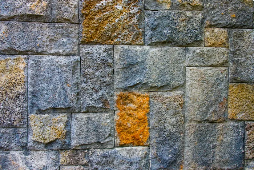 Close-up of a textured stone wall with grey and yellowish-brown rectangular stones, showcasing surface detailing.
