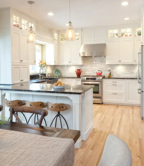 Modern kitchen with white cabinets, granite countertops, stainless appliances, and wooden dining table with stools.