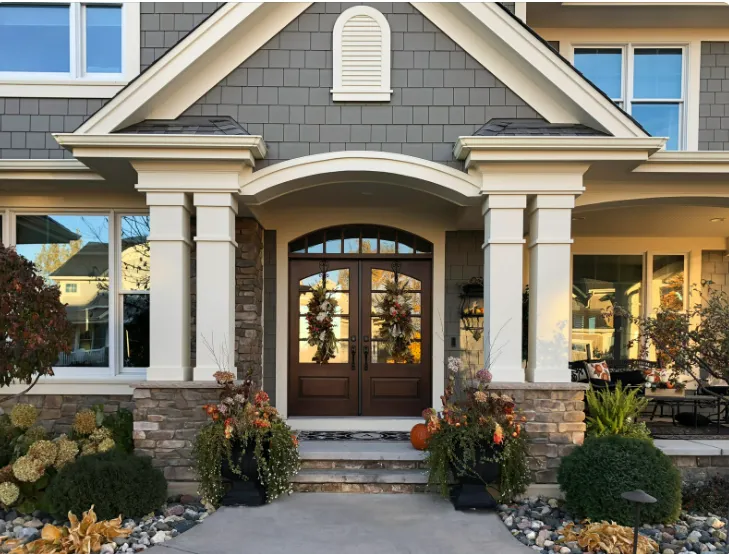 Charming entrance with double wooden doors, wreaths, potted plants, and autumn décor showcasing modern house exterior.