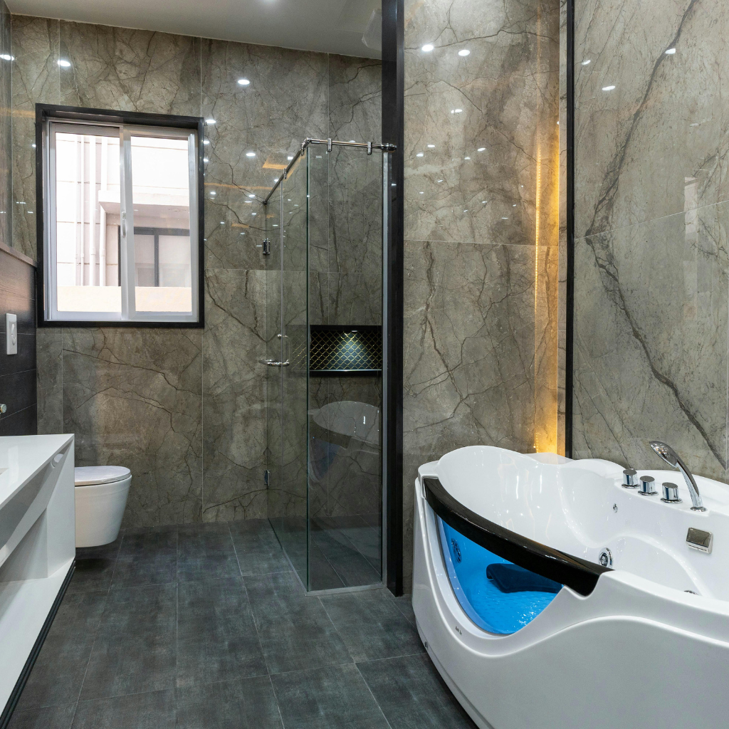 Luxury bathroom remodeling featuring floor-to-ceiling gray marble tiles, a walk-in glass shower, and a modern jetted soaking tub.