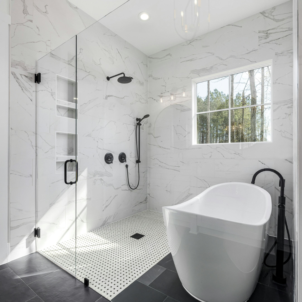 Modern bathroom remodeling featuring a walk-in glass shower with marble tile walls, black fixtures, and a white freestanding soaking tub.